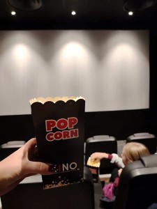 Henkilö pitää kädessään popcorn-rasiaa elokuvateatterissa